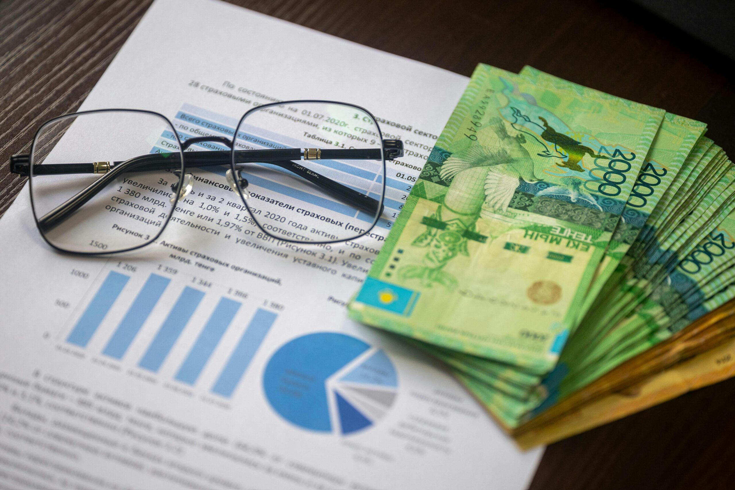 Kasachische Tenge-Banknoten und Finanzberichte auf einem Schreibtisch, die eine Finanzanalyse darstellen.