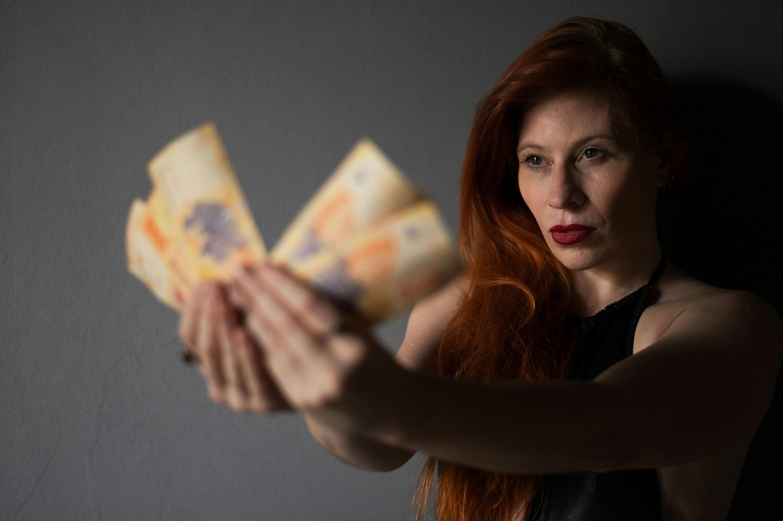Frau mit roten Haaren hält argentinische Peso-Scheine in einem Innenraum.