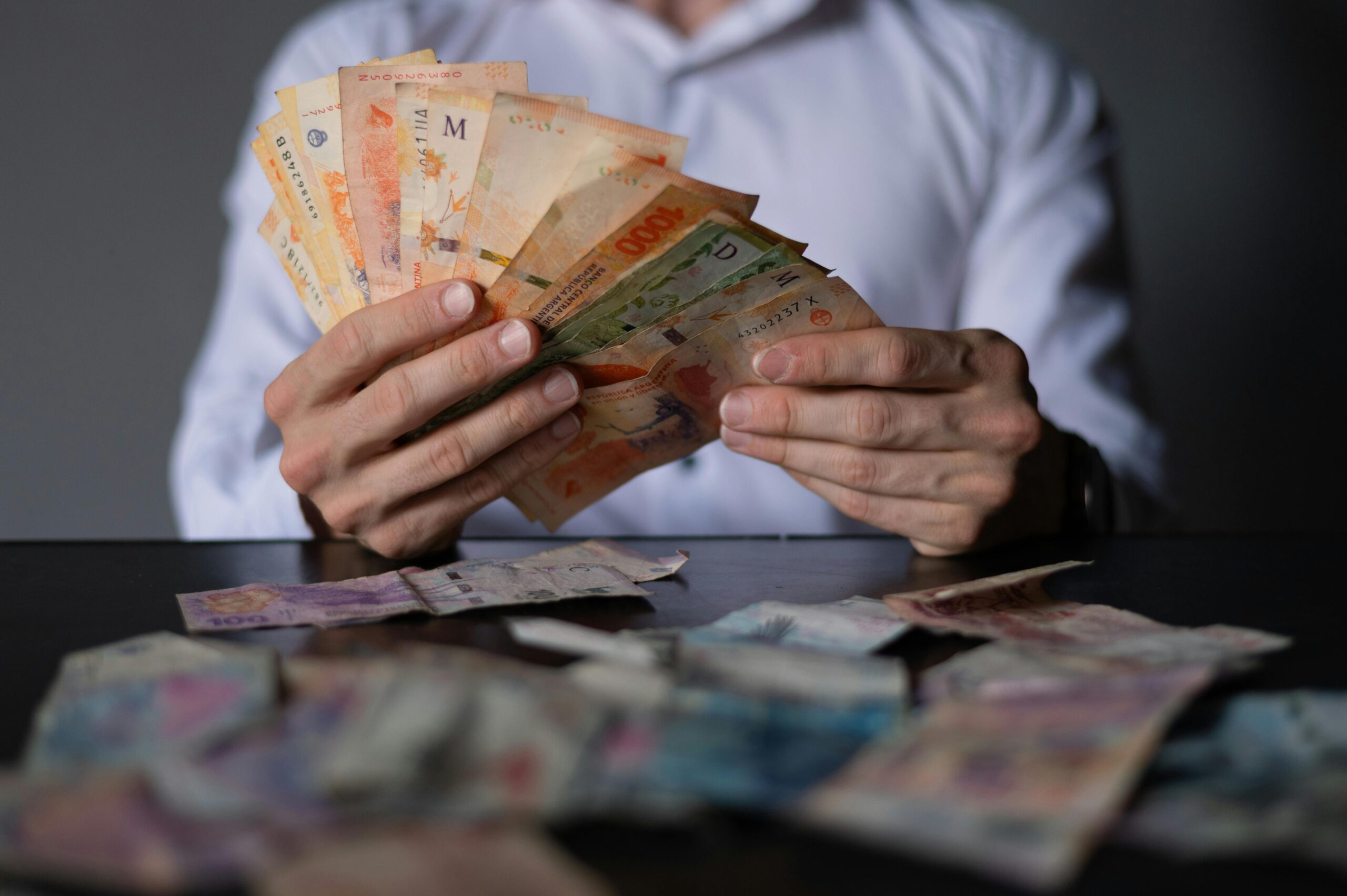 Nahaufnahme eines Mannes, der an einem Tisch argentinische Peso-Scheine zählt und dabei den Umgang mit Währungen erläutert.