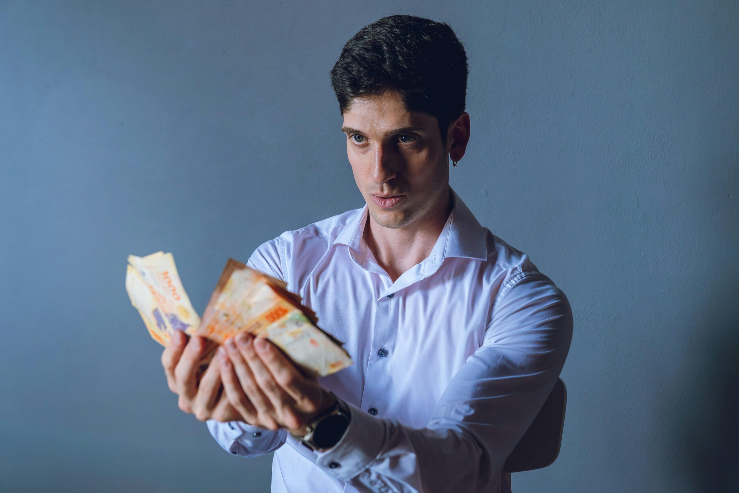Ein konzentrierter erwachsener Mann zählt argentinische Pesos in einem Innenraum vor einem neutralen Hintergrund.