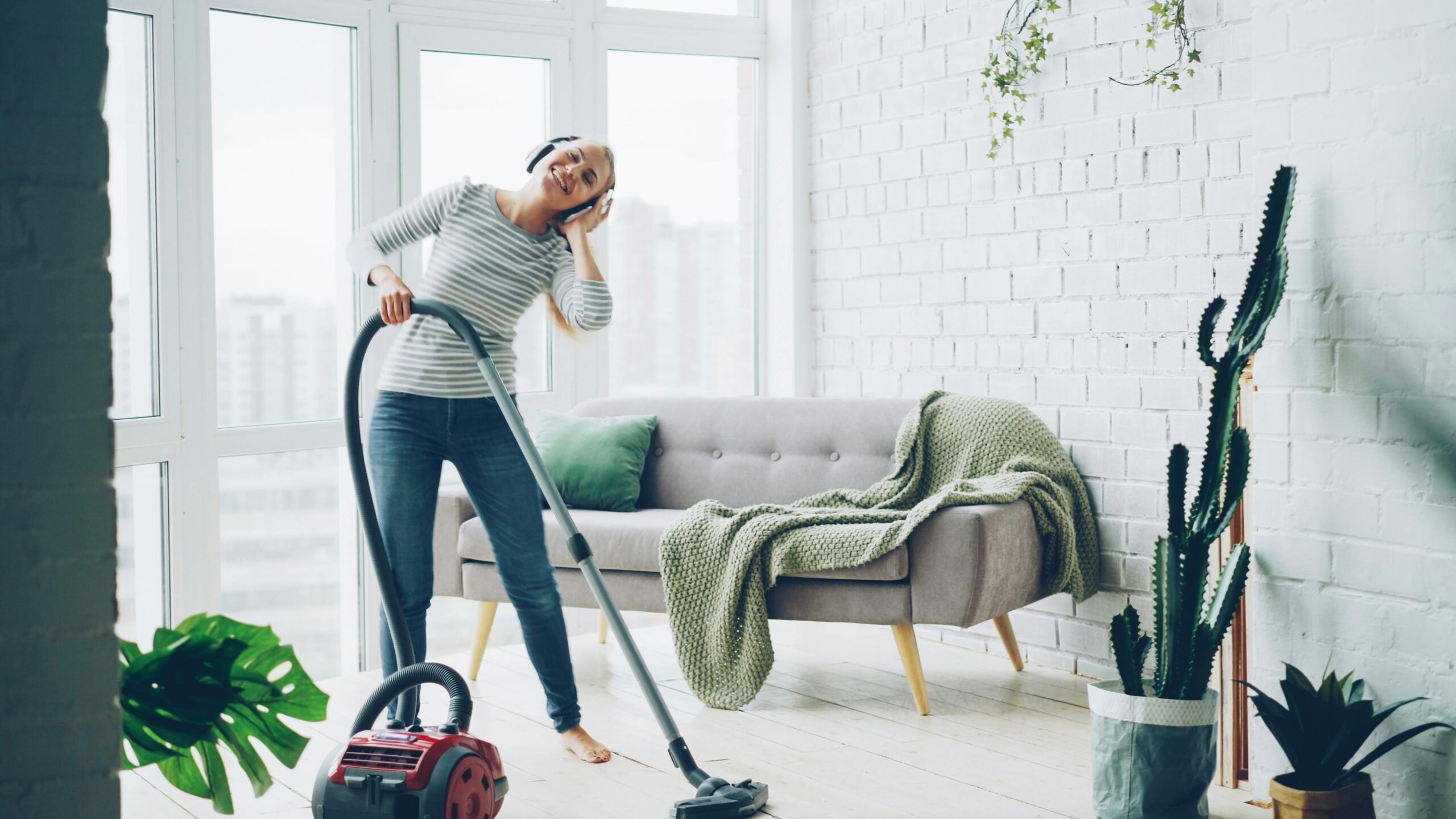 Eine glückliche Frau hört Musik, während sie ein stilvolles Wohnzimmer staubsaugt.